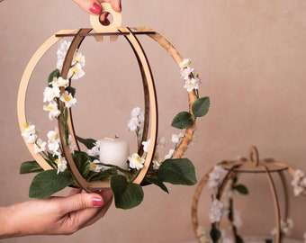 May include: Two round wooden candle holders with a delicate floral design. The holders are decorated with white flowers and greenery. A white candle is placed inside the holder on the left.