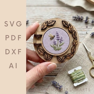 May include: A round wooden embroidery hoop with a lavender and bee design. The embroidery is set in a light purple fabric. The hoop is surrounded by laser-cut wooden leaves. The text "SVG PDF DXF AI" is on the left side.