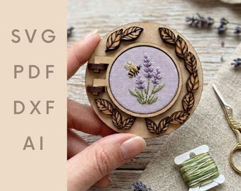 May include: A circular wooden embroidery hoop featuring a lavender and bee design. The embroidery is set in a pale purple fabric. The hoop is encircled by laser-cut wooden leaves. The text "SVG PDF DXF AI" is visible on the left.