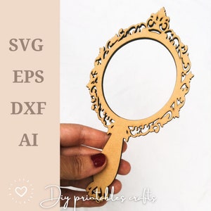 Puede incluir: Un recorte de madera de un espejo de mano con un marco decorativo adornado. El espejo se sostiene en una mano.