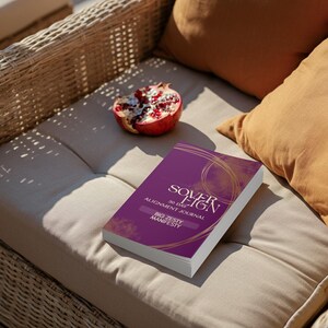 May include: A rectangular journal with a deep purple cover featuring gold circular line art and the text Sovereign 30 Day Alignment Journal Big Zesty Manifesty. The book is positioned next to a halved pomegranate showing red seeds and white pith.