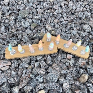May include: A set of ten almond-shaped press-on nails displayed on two rectangular bamboo stands. The nails feature various pastel colors including light blue, yellow, peach, and white, with some decorated with small white and yellow floral patterns.
