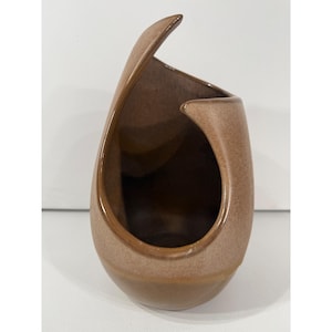 May include: A ceramic vase with a smooth, glossy brown finish and a unique asymmetrical, teardrop-shaped opening. The vessel features a curved, sweeping silhouette that tapers toward the top, with a deep, dark interior visible through the side cutout.