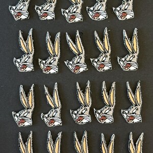 May include: A collection of twenty identical embroidered patches, each featuring the head of a cartoon rabbit with long ears, gray fur, white muzzle, and a brown nose, arranged in four rows of five on a dark background.