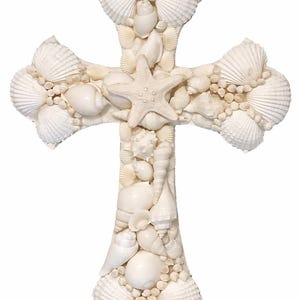 May include: A decorative cross crafted from various seashells, including scallop shells, conch shells, and a starfish at the center. The cross is white and has a textured surface, perfect for coastal or beach-themed decor.