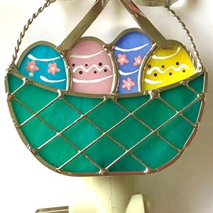 May include: A green and silver stained glass night light shaped like a basket with a bow on top. The basket contains four colorful Easter eggs.