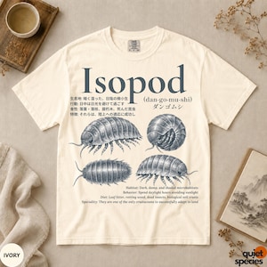 Puede incluir: Una camiseta de manga corta color marfil con un estampado gráfico azul oscuro de isópodos. El diseño incluye el texto Isopod (dan-go-mu-shi), caracteres japoneses y texto en inglés que detalla el hábitat, comportamiento, dieta y especialidad.