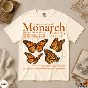 May include: An ivory short-sleeve t-shirt featuring a graphic print of four orange and black monarch butterflies. The design includes the text Monarch Butterfly, scientific facts in English and Japanese, and the phonetic spelling oo-ka-ba-ma-da-ra.