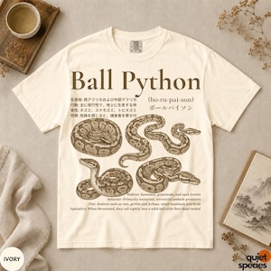 May include: An ivory t-shirt featuring a brown graphic print of ball pythons in various coiled positions. The text includes "Ball Python," Japanese characters, and English descriptions detailing the habitat, behaviour, diet, and special traits of the snake.