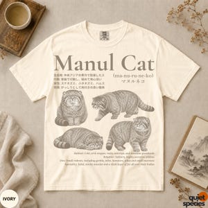 Könnte beinhalten: Ein elfenbeinfarbenes Kurzarm-T-Shirt mit einem braunen Grafikdruck von vier Manul-Katzen. Das Design enthält den Text 'Manul Cat', japanische Schriftzeichen sowie englische Beschreibungen zu Lebensraum, Verhalten, Ernährung und körperlichen Merkmalen.
