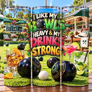 May include: A cylindrical tumbler featuring a lawn bowls theme with the text I LIKE MY BOWLS HEAVY & MY DRINKS STRONG. The design displays black lawn bowls, a white jack, a glass of whiskey with orange slices, and a cocktail with lime and mint.