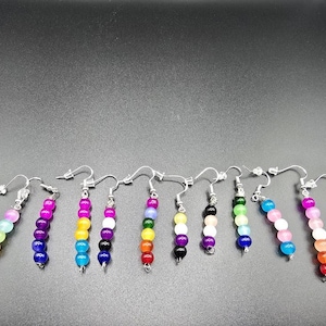 May include: A collection of ten individual dangle earrings, each featuring a vertical row of small, round, multi-colored beads suspended from silver-toned metal hooks. The beads display various color combinations including pink, blue, yellow, purple, green, and white.