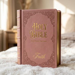 May include: A dusty rose-colored Holy Bible, King James Version, featuring gold foil lettering and ornate embossed scrollwork borders on the front cover. The word Faith is inscribed in gold at the bottom, and the page edges are finished in gold.