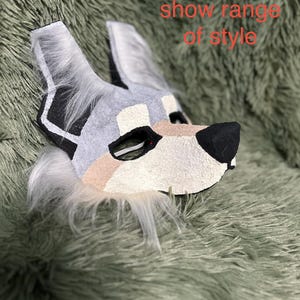 May include: A wolf-like animal mask featuring grey, white, and tan textured panels with black accents around the eyes and nose, and white faux fur trim. The text "WIP! Used to show range of style" is visible in red on the upper right side.