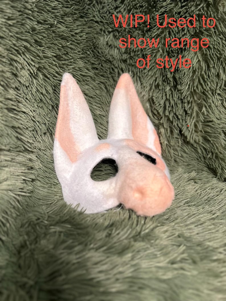 May include: A white and peach-colored animal mask with tall pointed ears and a snout, featuring black-lined eye openings. The text 'WIP! Used to show range of style' is printed in red across the upper portion of the image.