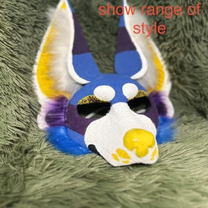 May include: A blue, white, purple, and yellow animal-themed mask with tall, pointed ears and textured fur accents. The mask features a yellow nose and eye markings, with the text WIP! Used to show range of style printed in red over the top.