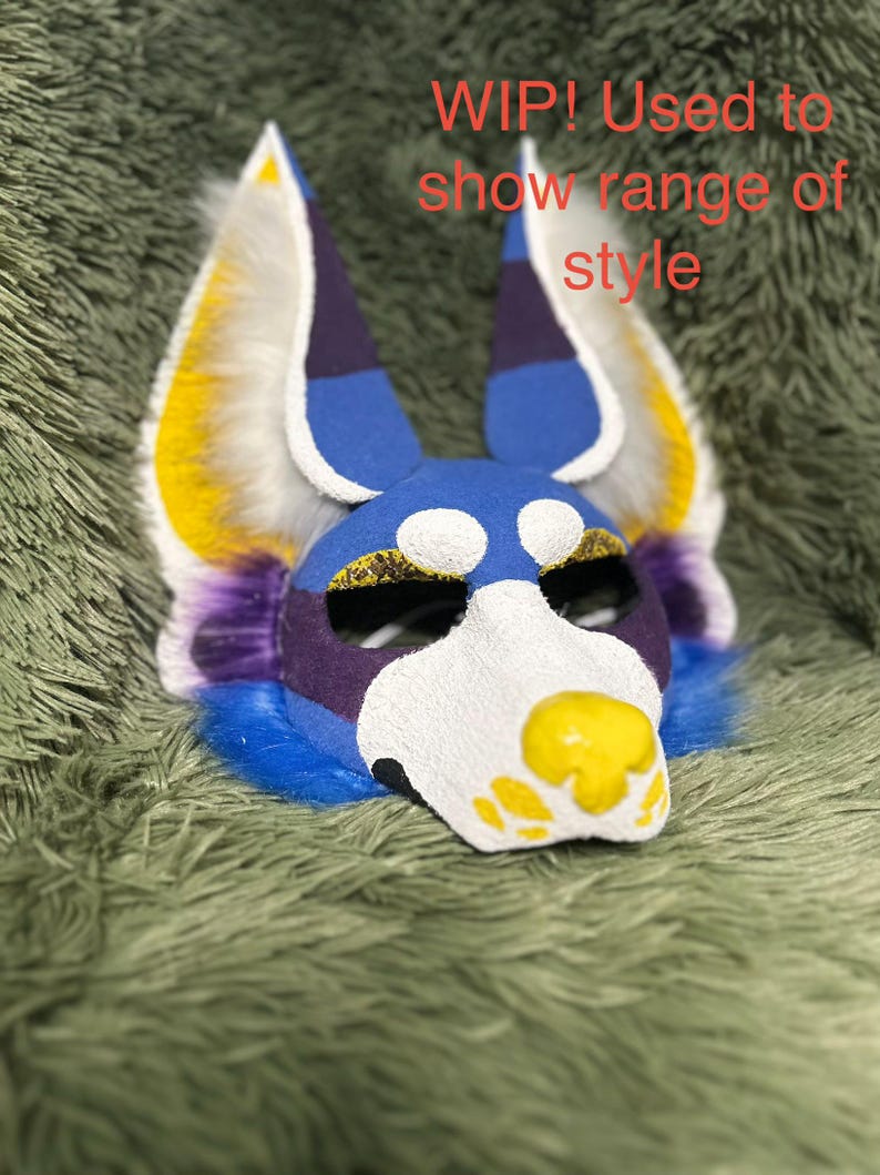 May include: A blue, white, purple, and yellow animal-themed mask with tall, pointed ears and textured fur accents. The mask features a yellow nose and eye markings, with the text WIP! Used to show range of style printed in red over the top.