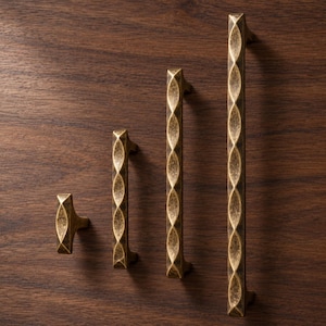 May include: A collection of four antique brass cabinet hardware pieces, including one small knob and three elongated drawer pulls of varying lengths. Each piece features a repeating, textured, diamond-shaped pattern along the front surface.