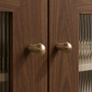 Puede incluir: Un armario de madera oscura con dos puertas que tienen paneles de vidrio estriado vertical y pequeños pomos de latón redondeados. El armario está rematado con una superficie de piedra gris claro lisa, y se ven platos blancos apilados tras el cristal.