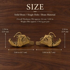 May include: Two solid brass anglerfish-shaped cabinet knobs. Each knob measures 6.7 cm in width and 3.9 cm in height, with a thickness of 2.6 cm. The pair weighs 170.6 g. The text reads SIZE, Solid Brass, Single Hole, Brass Material.
