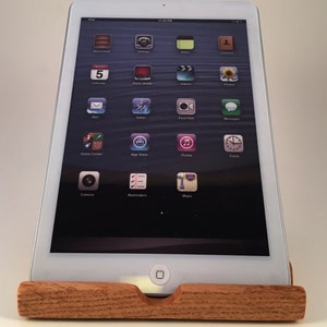 May include: A white iPad tablet with a black screen displaying the home screen with various app icons. The tablet is resting on a wooden stand.