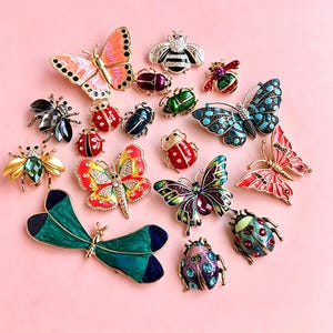 May include: A collection of insect and butterfly shaped brooches featuring various colors including pink, blue, green, red, and purple. The pins are decorated with enamel, metallic finishes, and small clear crystals in diverse patterns and sizes.