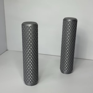 May include: Two cylindrical handles in a dark gray finish, each featuring a prominent diamond-shaped knurled texture across the entire surface. The handles are upright, showing a flat top and a slightly tapered base, with a consistent matte appearance.