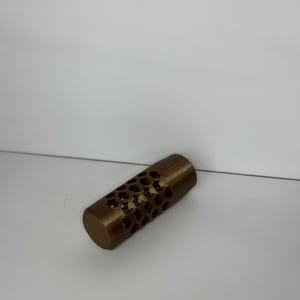 May include: A cylindrical object with a metallic bronze finish featuring a repeating hexagonal honeycomb pattern cut out along the center section. The ends of the cylinder are solid and smooth, providing a contrast to the open geometric lattice design.