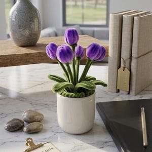 May include: A small potted plant featuring five vibrant purple tulip-shaped blossoms with soft, fuzzy textures. The flowers have green stems and leaves, and are set in a simple, smooth white ceramic pot. The plant is displayed on a white marble surface.