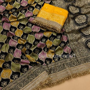 May include: A black fabric with a repeating scalloped pattern in shades of mustard yellow, olive green, and lavender, featuring intricate floral motifs. A folded mustard yellow textile with a wide gold border and fringe trim rests on top.