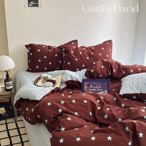 May include: A bedding set featuring a deep maroon duvet cover and matching pillowcases adorned with a repeating pattern of small, light blue stars. The set includes a light blue fitted sheet and a tablet displaying the text Work & Study Jazz.
