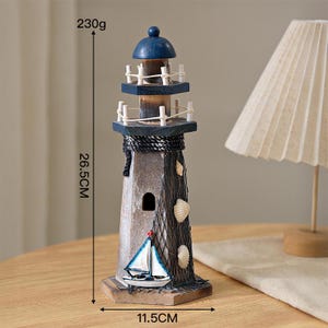 May include: A wooden lighthouse figurine featuring a blue dome, white railings, and a dark brown body. It is decorated with a black fishing net, white seashells, and a small sailboat model. It measures 26.5 cm in height, 11.5 cm wide, and weighs 230g.