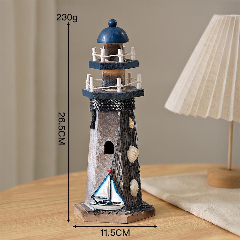 May include: A wooden lighthouse figurine featuring a blue dome, white railings, and a dark brown body. It is decorated with a black fishing net, white seashells, and a small sailboat model. It measures 26.5 cm in height, 11.5 cm wide, and weighs 230g.