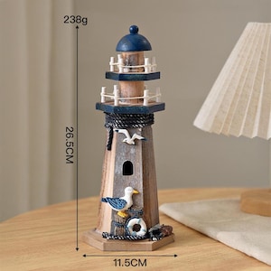 May include: A wooden lighthouse figurine featuring a blue dome top, white railings, and a dark rope accent. The structure is decorated with a seagull and a life ring. It measures 26.5 cm in height, 11.5 cm in width, and weighs 238 grams.