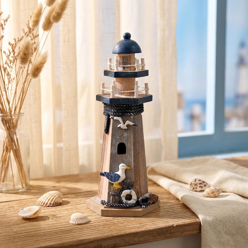 May include: A wooden lighthouse figurine featuring a dark blue dome, two railed balconies, and a natural wood finish. The structure is decorated with a black rope accent, a white seagull figure, and a small life preserver ring at the base.