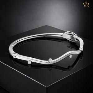 May include: A silver-toned wavy bangle bracelet featuring a polished metallic finish and four evenly spaced round clear stones set along the outer edge. The bracelet includes a secure hinged clasp mechanism at one end for closure.
