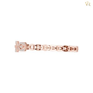 May include: A rose gold ring featuring a repeating openwork leaf-like pattern along the band. The focal point is a rectangular section adorned with small, clear, round-cut stones set in a geometric arrangement, creating a delicate and refined appearance.