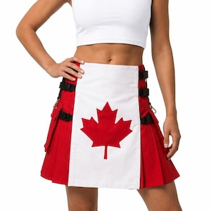 Op de afbeelding: Een rood-witte kilt met een centraal wit paneel voorzien van een groot rood esdoornbladontwerp. Het kledingstuk bevat zijzakken, zwarte verstelbare banden met plastic gespen aan beide kanten en een geplooide rokconstructie.