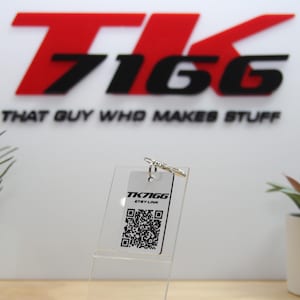 May include: A rectangular white acrylic keyring featuring a black printed QR code, the text TK7166, and the text ETSY LINK. The keyring is attached to a silver metal split ring and is displayed on a clear acrylic stand for visibility.