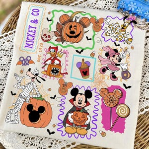May include: A white tote bag featuring a colorful Halloween-themed print with Disney characters including Mickey Mouse as a vampire, Minnie Mouse as a witch, Donald Duck as a devil, and Goofy as a mummy, alongside pumpkins, candy corn, and the text MICKEY & CO.