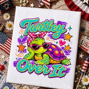 May include: A white canvas print featuring a green turtle wearing pink cat-eye sunglasses and a pink polka-dot headscarf. The text reads "Turtley Over It" in bright teal letters, surrounded by orange stars, a pink heart, and purple brush strokes.