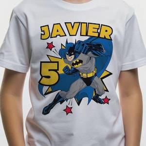 Op de afbeelding: Een wit t-shirt met korte mouwen en een afbeelding van Batman in een dynamische actiehouding. Het ontwerp bevat de naam JAVIER in gele blokletters, een groot geel cijfer 5, een blauwe cape en verschillende kleine rode sterren.