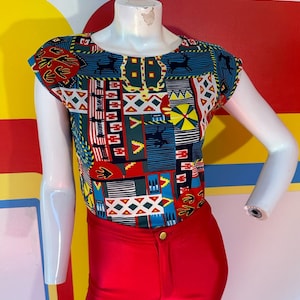 May include: A red, blue, green, yellow, and black patterned short-sleeved shirt with a round neckline. The shirt is on a white mannequin. The mannequin is wearing red pants.