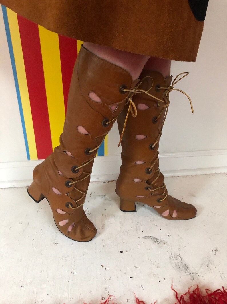 May include: Brown leather knee-high boots with cutouts and lace-up detail. The boots have a chunky heel and a pointed toe.