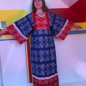 May include: A long blue and red dress with a white trim and a bandana print. The dress has long sleeves and a loose fit.