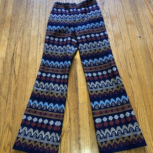 Könnte beinhalten: Marineblaue Hose mit Muster und ausgestelltem Bein. Die Hose hat ein sich wiederholendes geometrisches Design in Weiß, Orange und Gold. Die Hose ist aus einem gewebten Stoff und scheint Vintage zu sein.