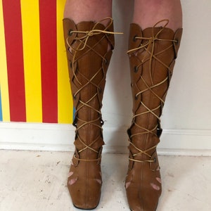 May include: A pair of brown leather knee-high boots with lace-up detailing. The boots have a square toe and a low heel.