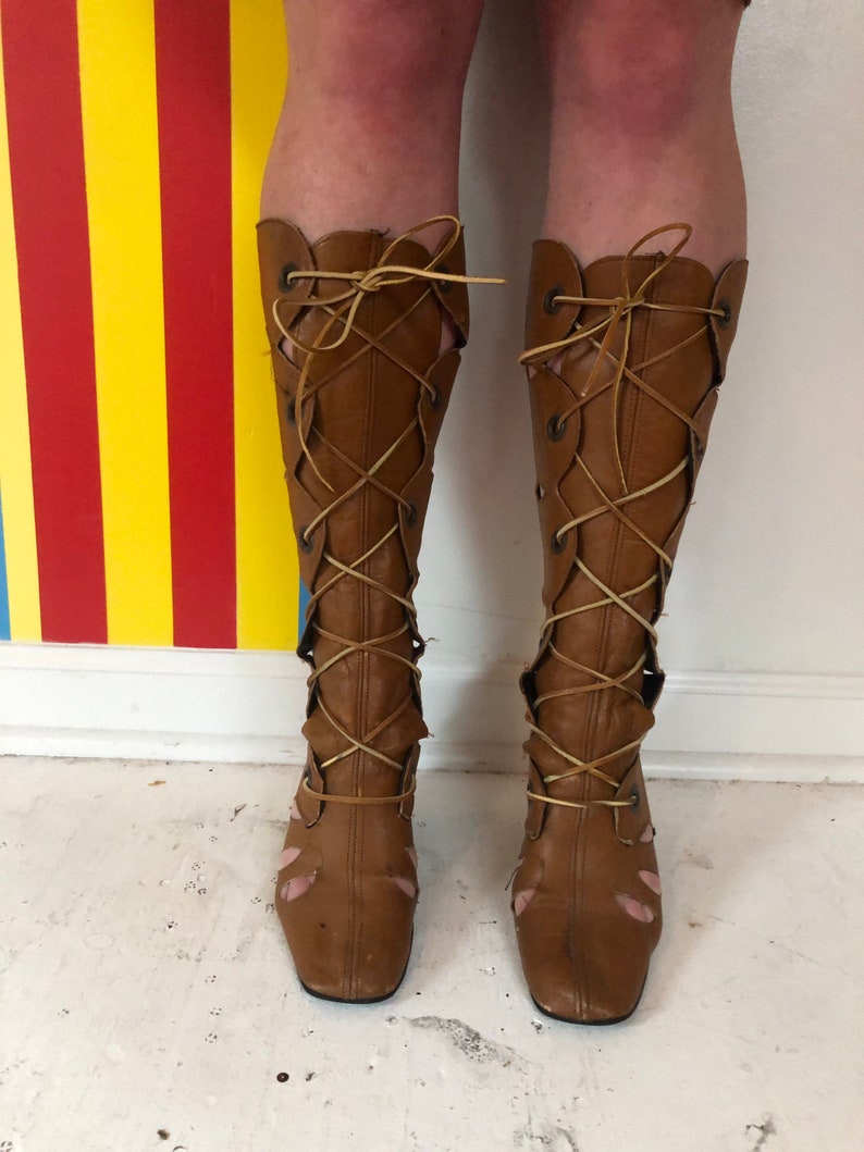 May include: A pair of brown leather knee-high boots with lace-up detailing. The boots have a square toe and a low heel.