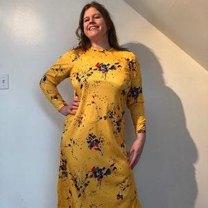May include: A yellow midi dress with a floral print in shades of red, blue, and green. The dress has long sleeves and a round neckline.
