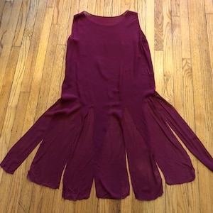 May include: A burgundy sleeveless dress with a sheer fabric and a split hem. The dress has a simple design and is made of a lightweight material.
